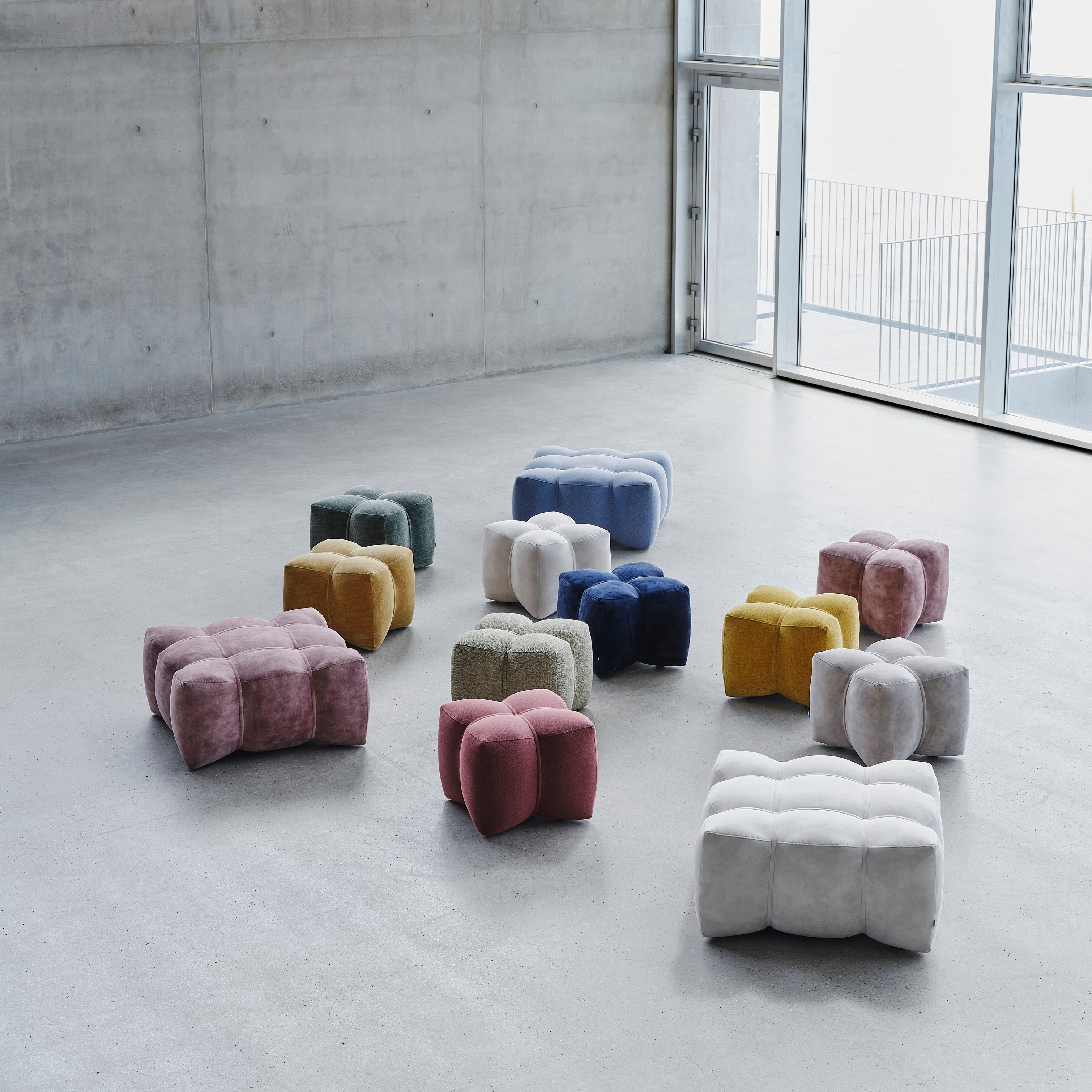 Variety of NaWABARI poufs in a modern, airy space with concrete walls and daylight.