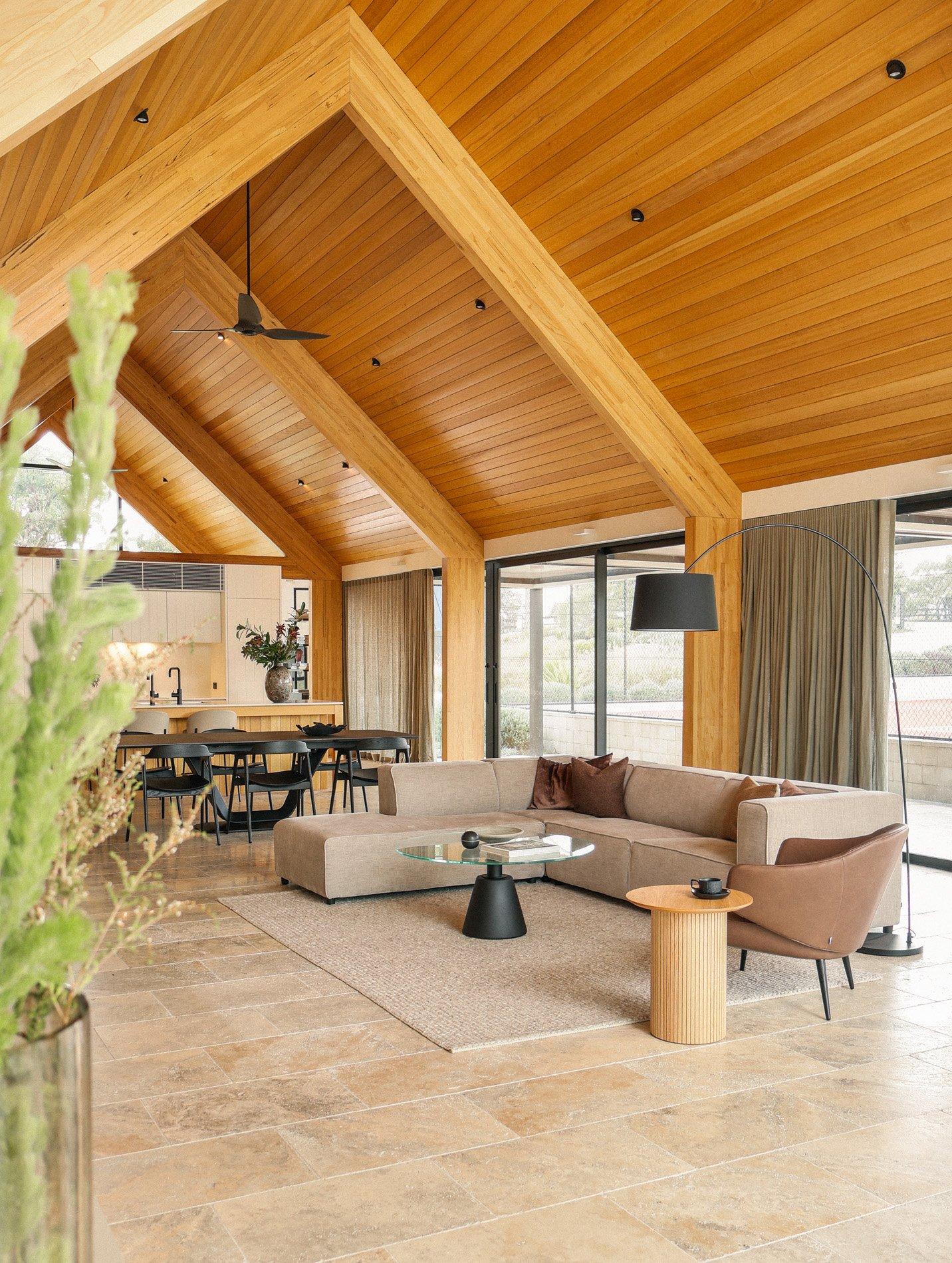Open-plan living room with curved sofa, glass coffee table and dining area under timber ceiling.