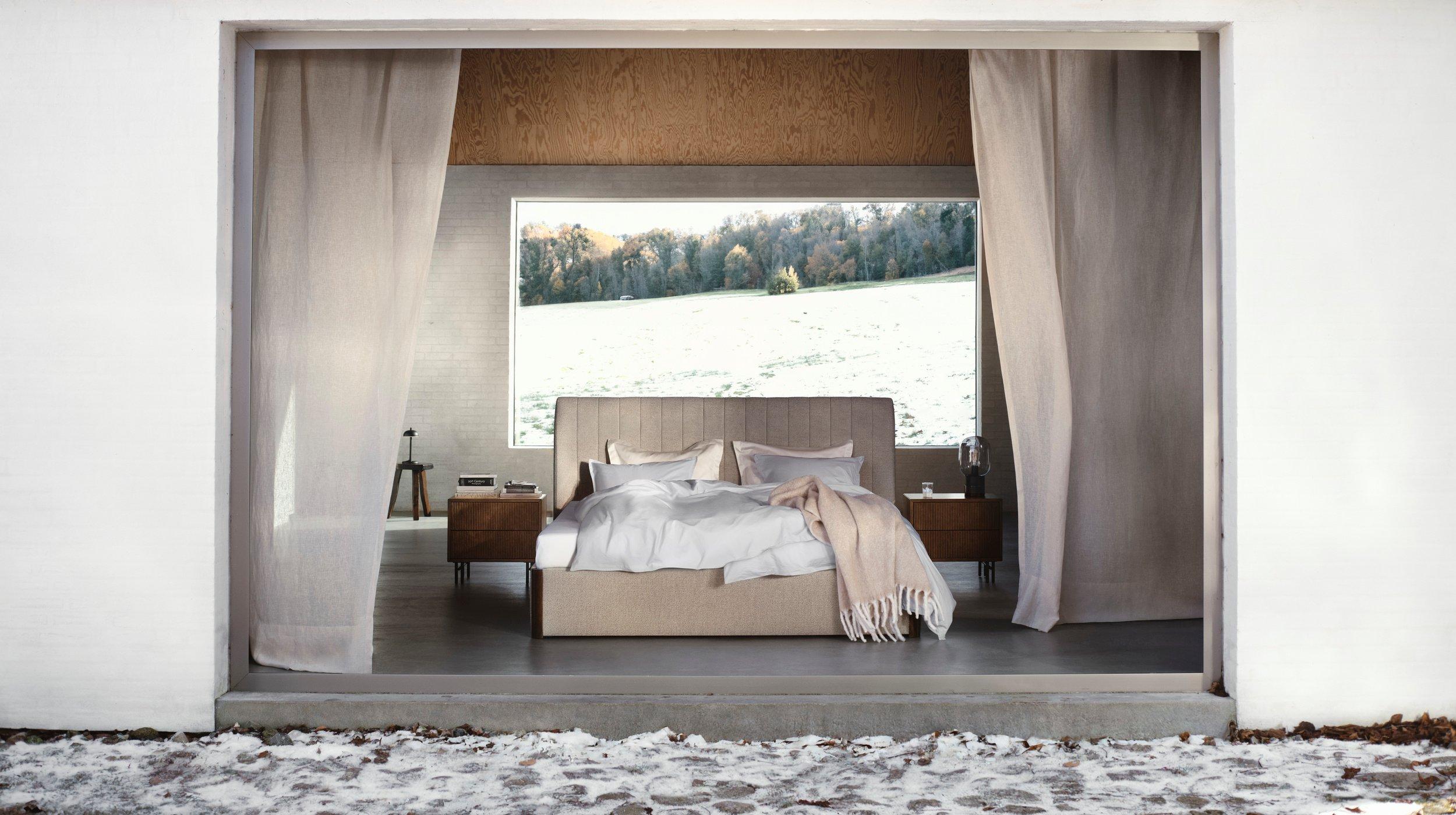 Minimalist bedroom with a low-profile Element bed, light bedding, and wooden Element nightstands, viewed through open curtains in a white structure.