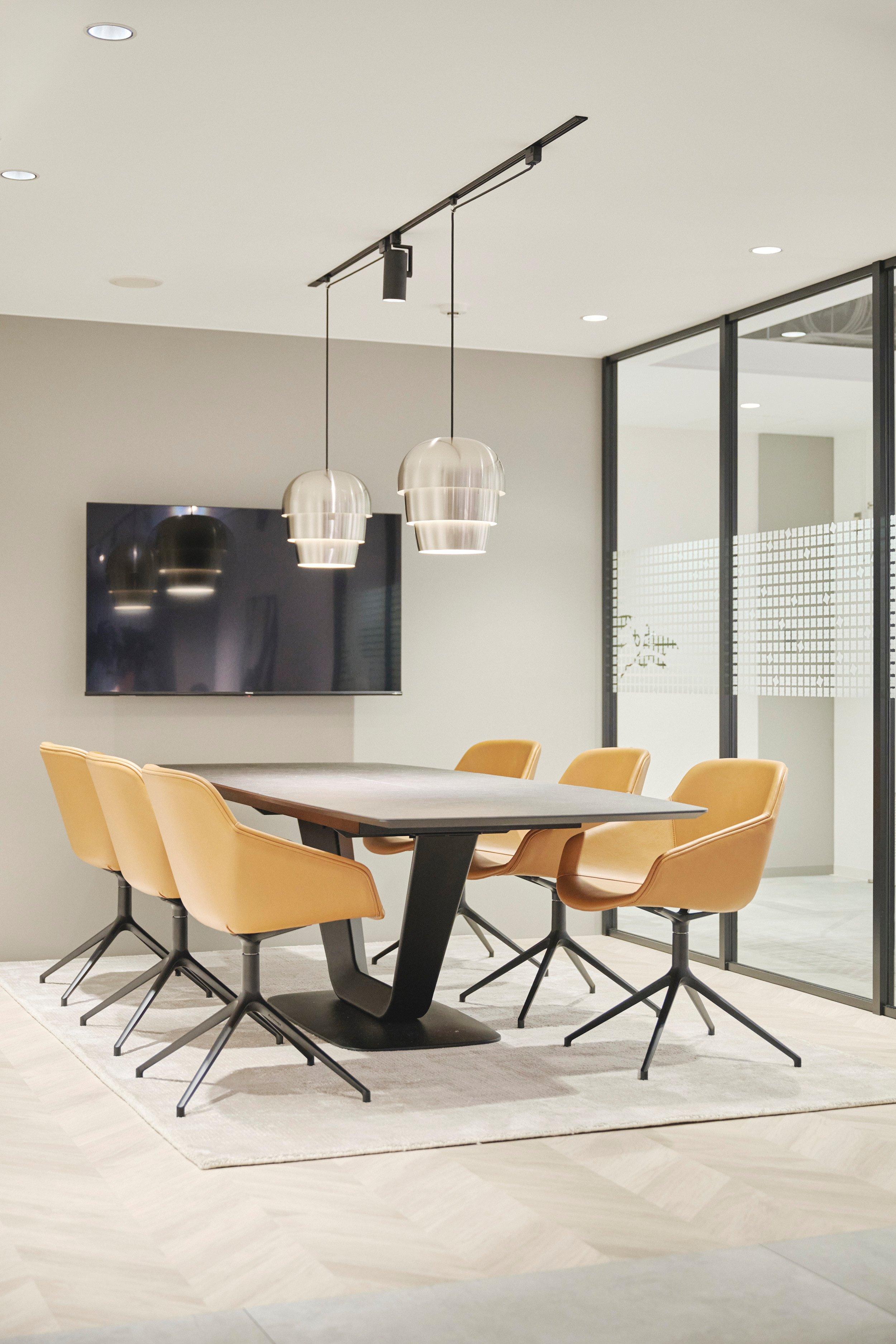 Sala de reuniones moderna con mesa, seis sillas de cuero y lámparas colgantes. Pantalla en la pared.