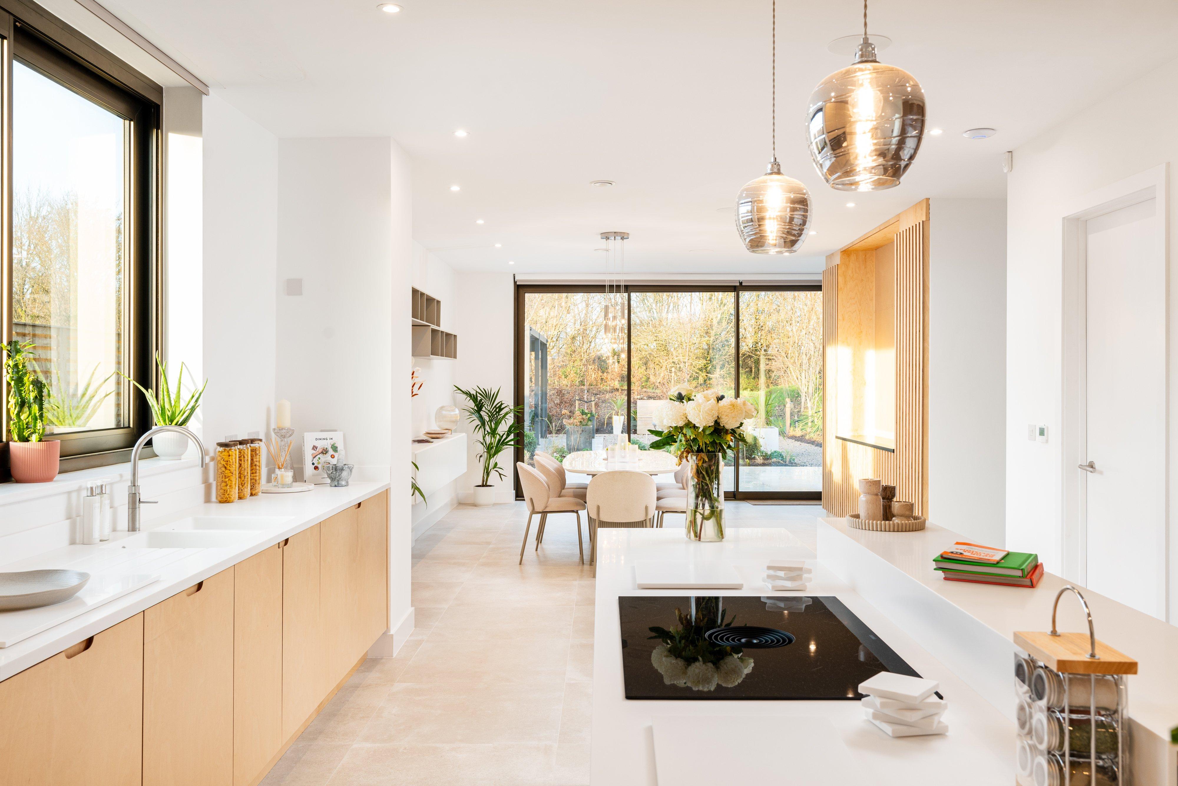 Modern kitchen with island hob, pendant lights and dining table by large sliding glass doors.