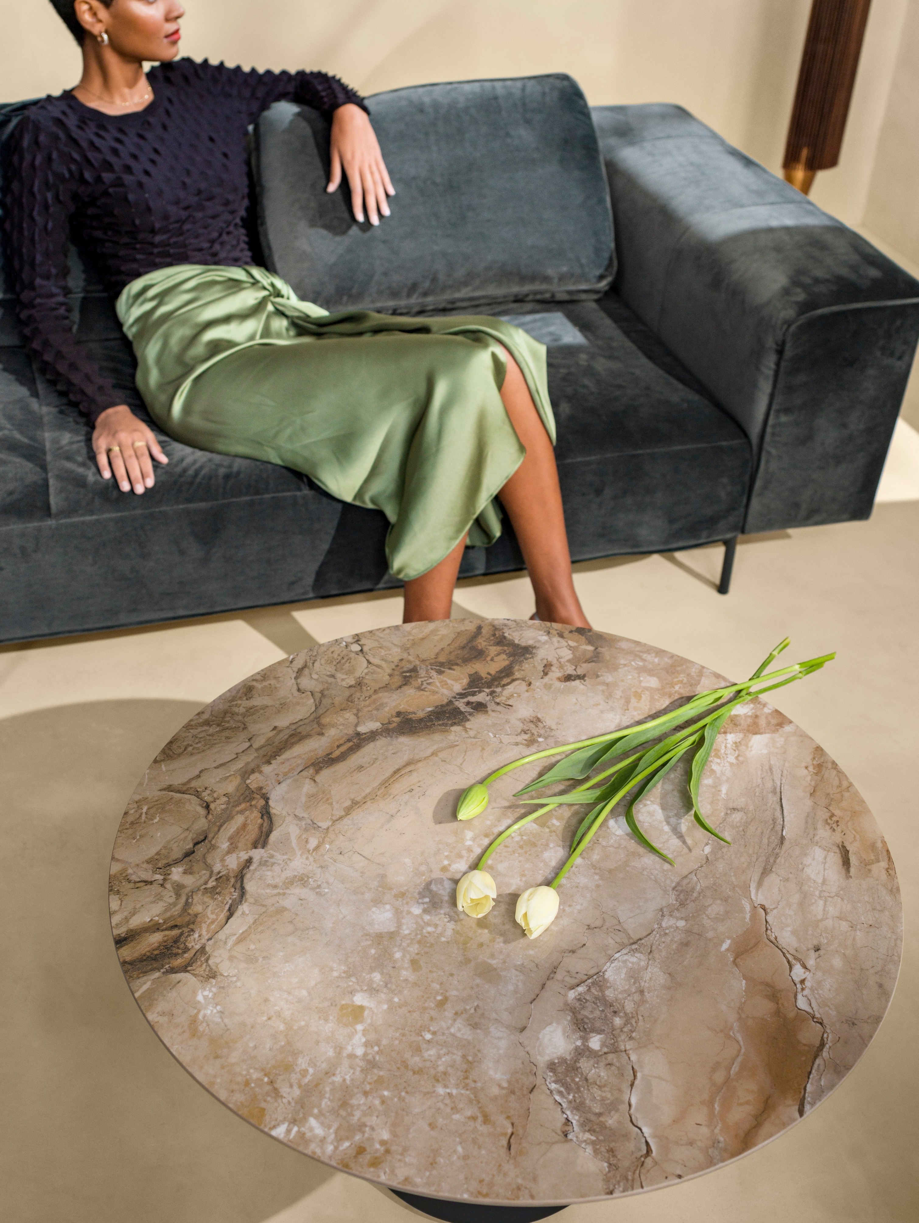 Woman sitting on the Amsterdam corner sofa next to the Madrid coffee table in ash ceramic