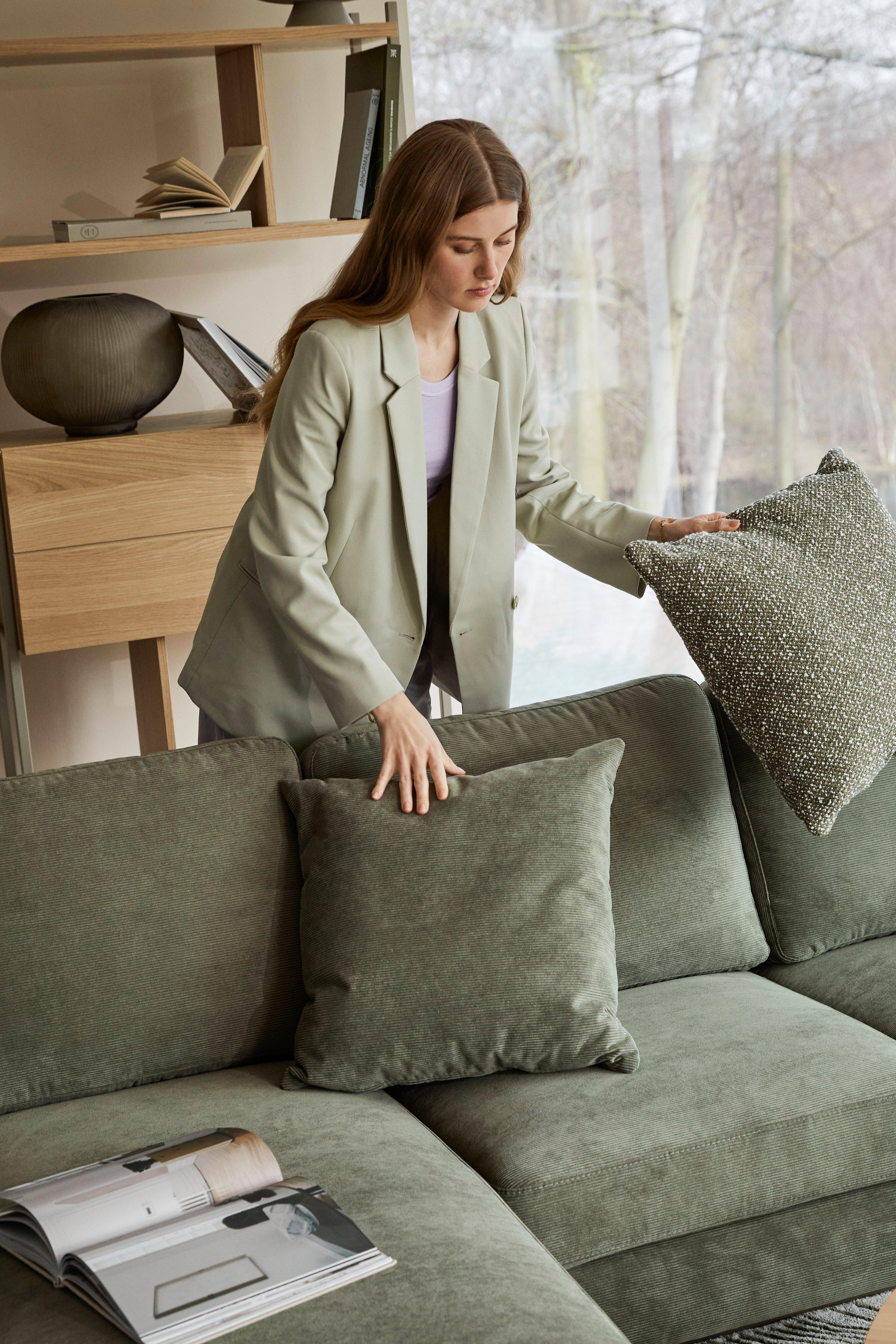 Woman adjusting green pillows on a matching green Indivi sofa in a living room with Calgary storage and a large window.