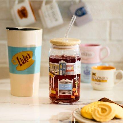 Glass jar with lid and straw filled with red drink, with a Luke’s cup and cookies nearby.