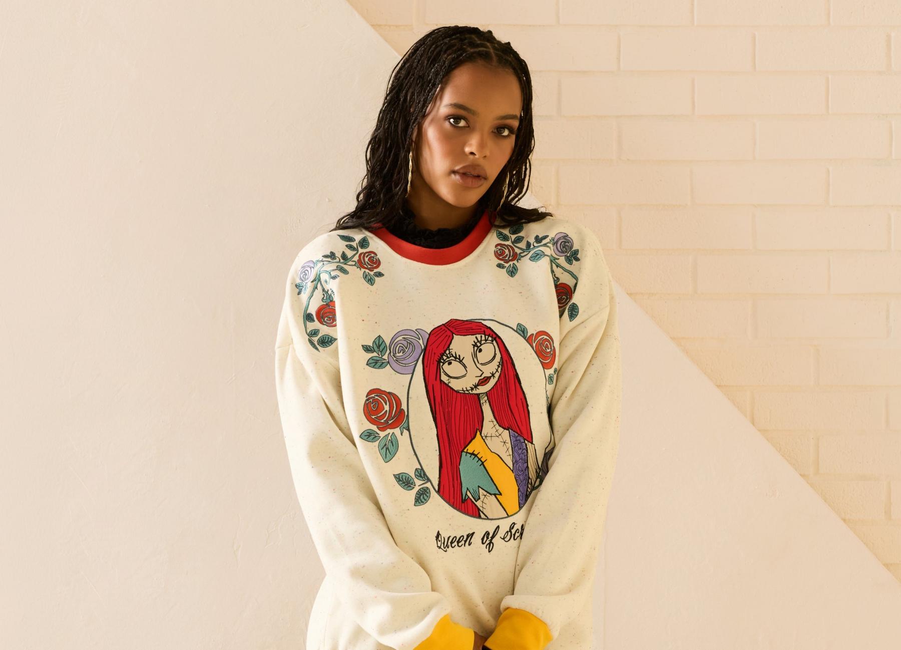 Model wearing a sweatshirt with floral print and Sally character graphic on the front and “Queen of Scream” text. Shop now.