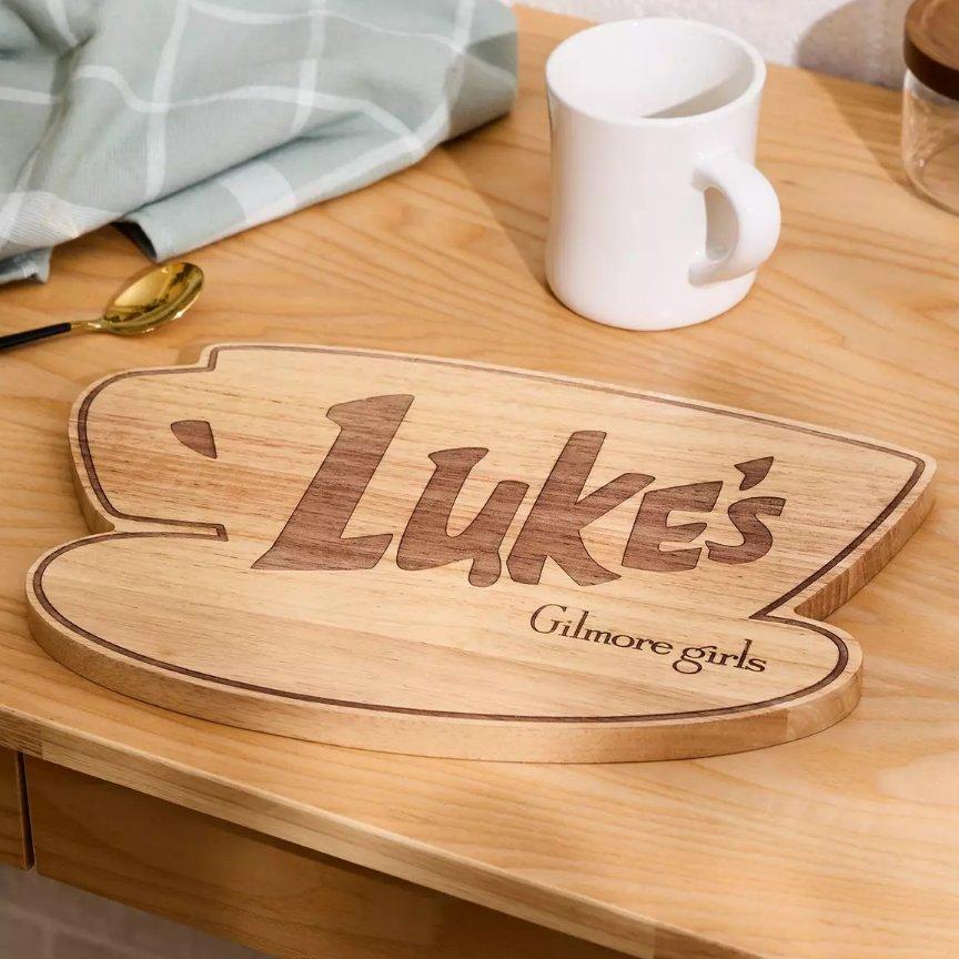 Wooden cutting board engraved with “Luke’s” and “Gilmore girls” on a tabletop. Shop Now.