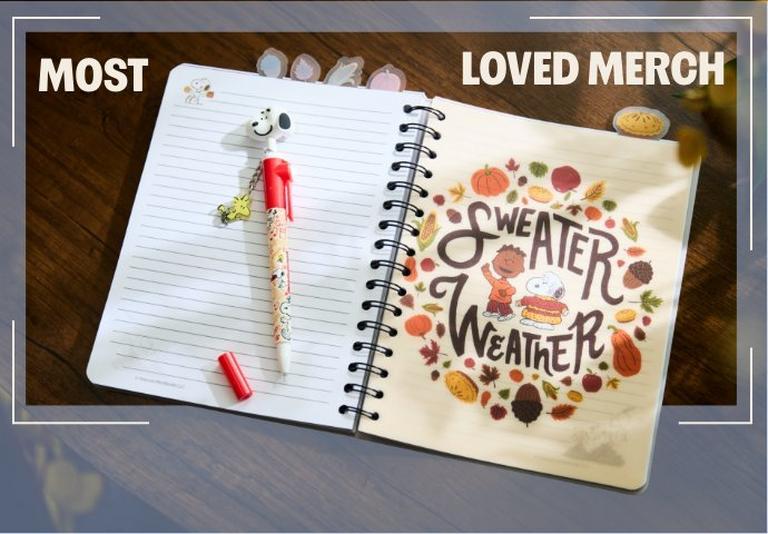 Open spiral notebook with Snoopy pen, tabbed dividers, and “SWEATER WEATHER” cover text. Shop Now.