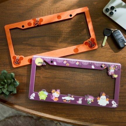 Two decorated license plate frames, one orange and one purple, on a table near car keys.