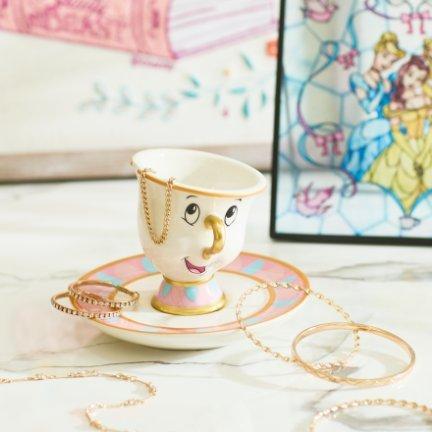 Chip teacup and saucer holding gold-tone jewelry chains and bangles.
