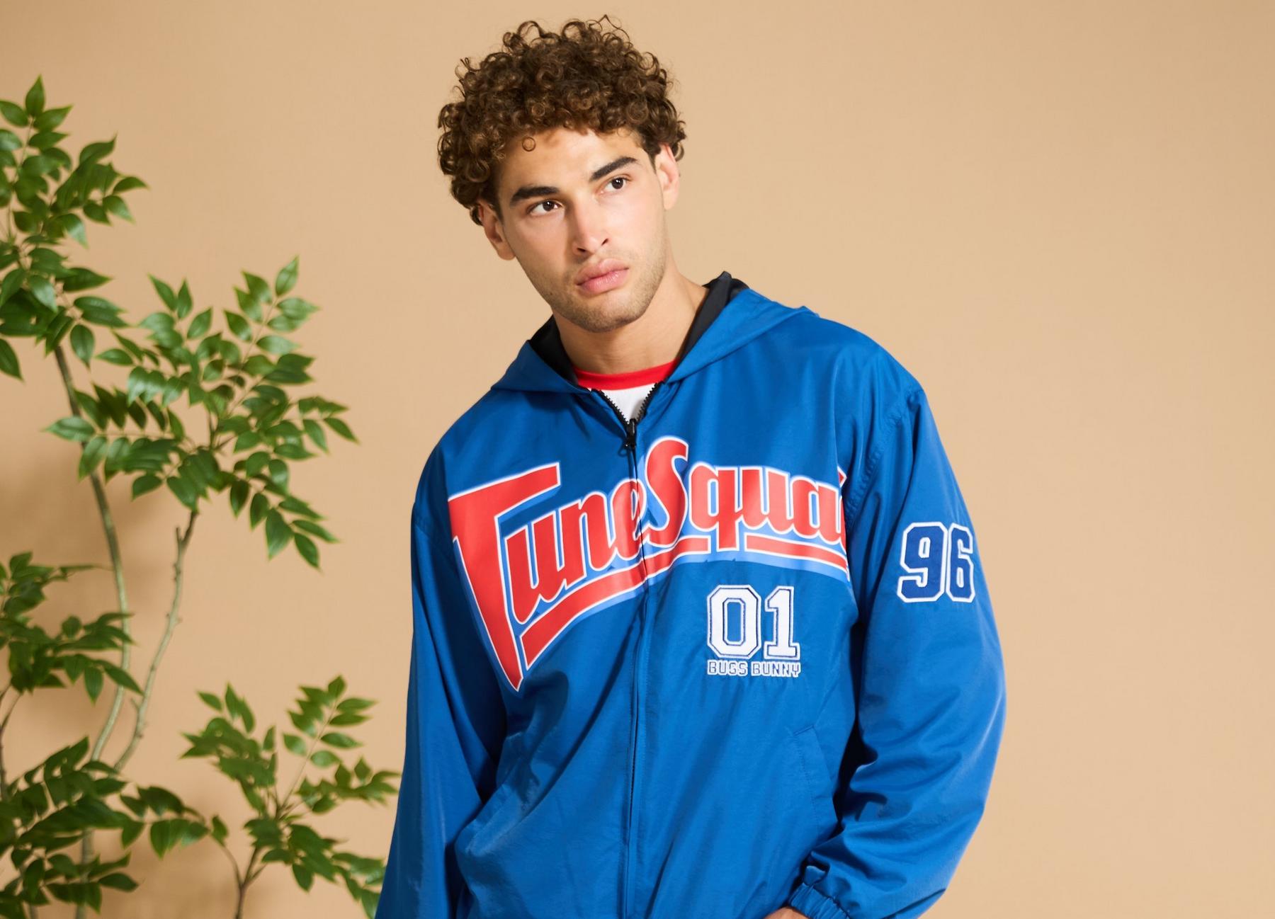 Model wearing a blue Tune Squad zip-up hooded jacket with Bugs Bunny 01 and 96 patches. Shop Now.