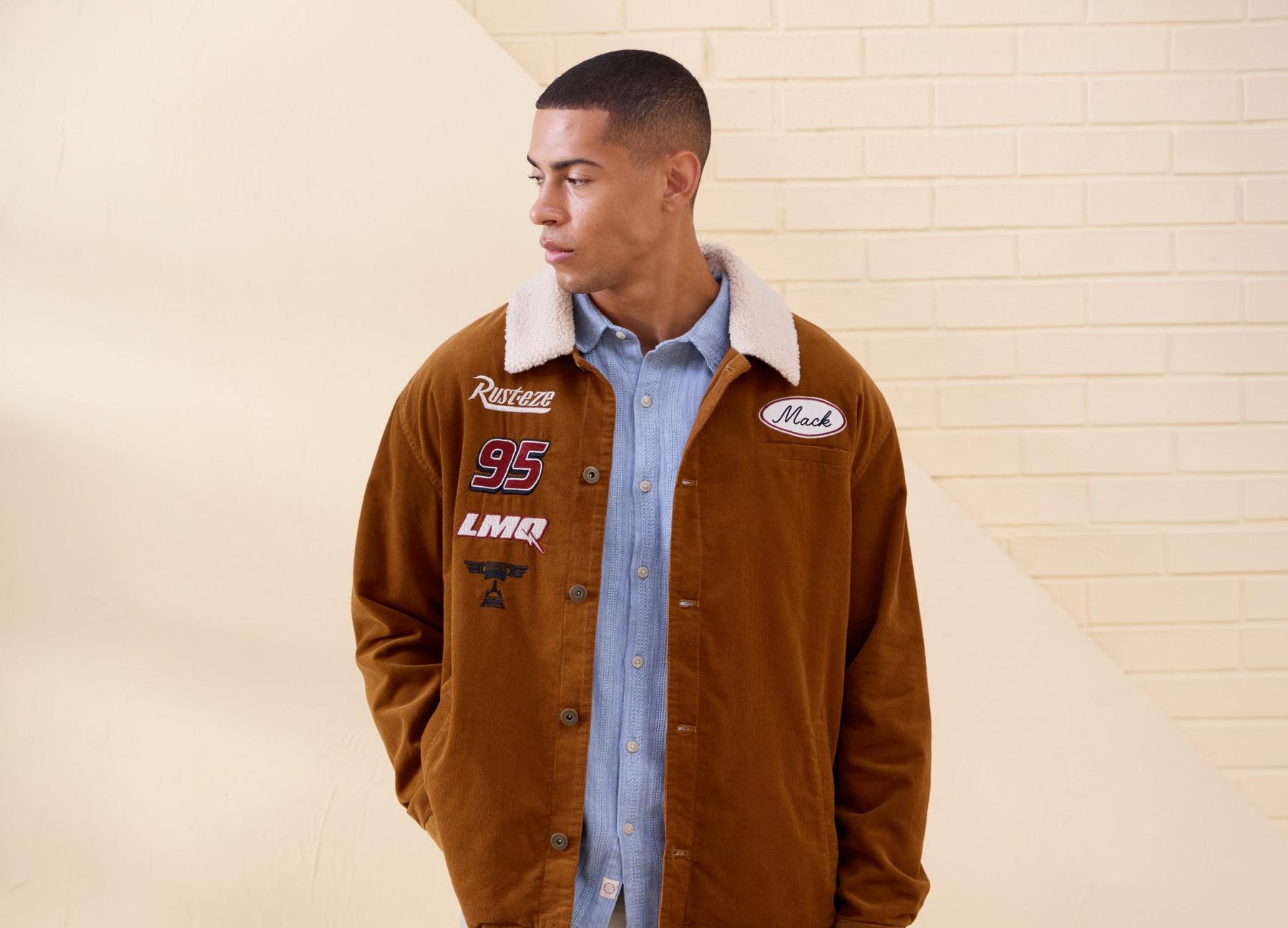 Model wearing a brown sherpa-collar jacket with Mack, Rust-eze, 95, and LMQ patches. Shop Now.