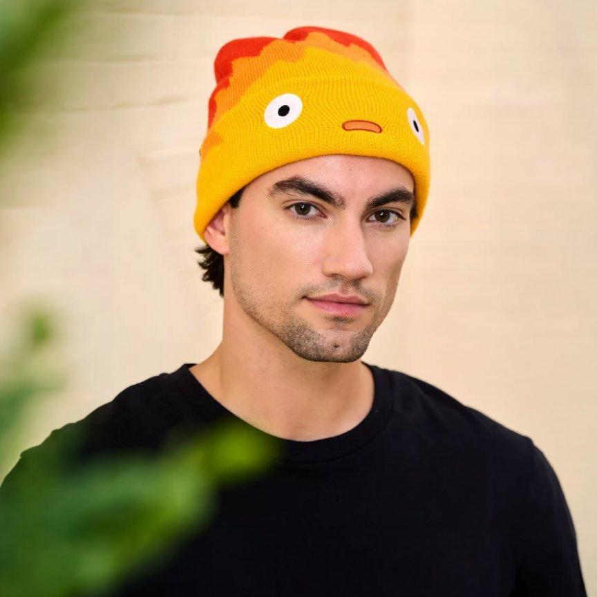 Man wearing a yellow knit beanie with Calcifer face design. Shop Now.