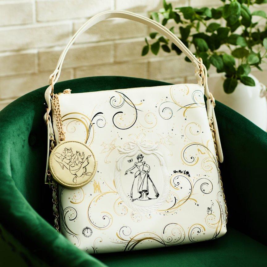 White Disney x Diferdinando shoulder bag with gold swirls and Cinderella illustration, with round charm on chain. Shop Now.