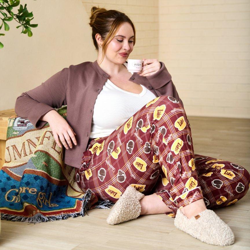Woman lounging in Luke’s pajama pants and slippers, sipping coffee from a Gilmore Girls mug. Shop Now.
