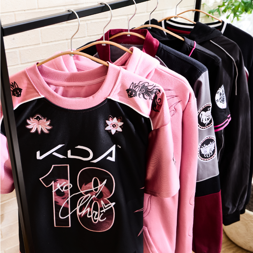 Pink and black KDA jersey with graphic details hanging on a clothing rack. Shop Now.