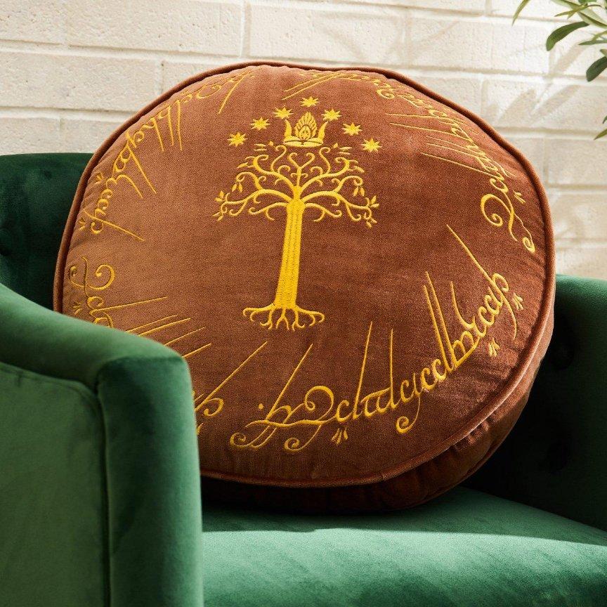 Round brown pillow with gold Tree of Gondor and decorative script embroidery. Shop Now.