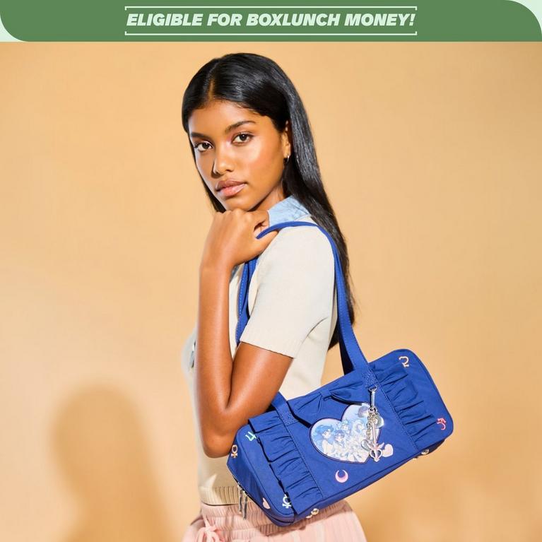 Model holding a blue Sailor Moon shoulder bag with a heart graphic patch and dangling charm under “ELIGIBLE FOR BOXLUNCH MONEY!” banner. Shop Now.