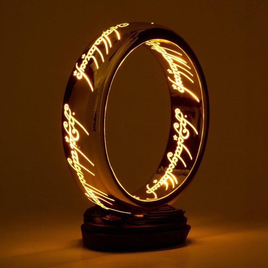 Glowing ring-shaped Lord of the Rings lamp with Elvish script cutouts on a small base. Shop Now.