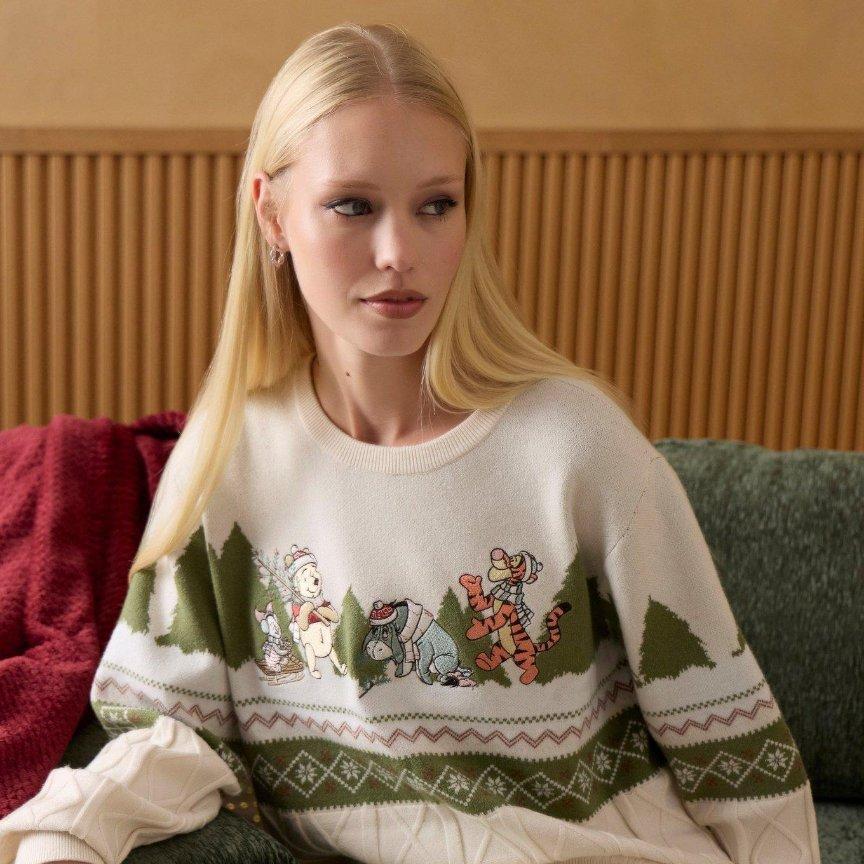 Woman wearing a holiday sweater with Winnie the Pooh, Piglet, Eeyore, and Tigger graphic. Shop Now. 