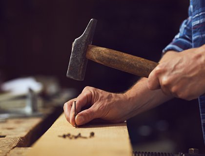 En person ska spika i en spik med hammare in en bräda 