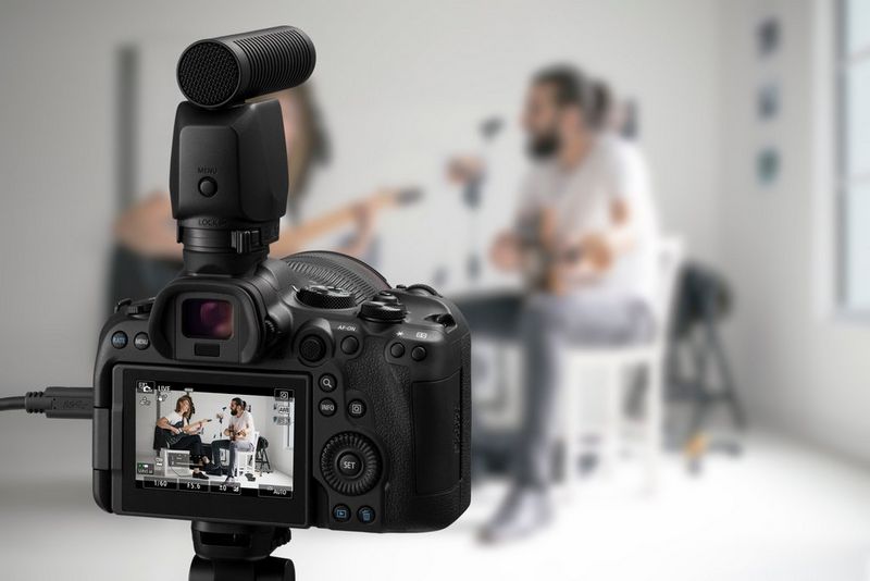 Een Canon EOS R6 Mark II-systeemcamera met Canons externe stereo-richtmicrofoon DM-E1D waarmee een videopodcast wordt opgenomen van twee mensen die op een elektrische gitaar spelen.