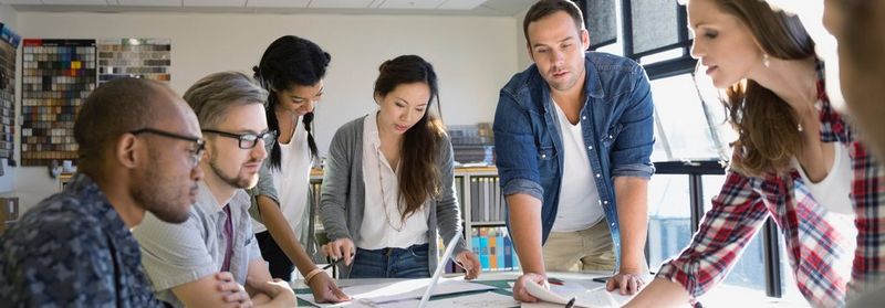 Casually dressed office workers huddle round a table to look through documents.