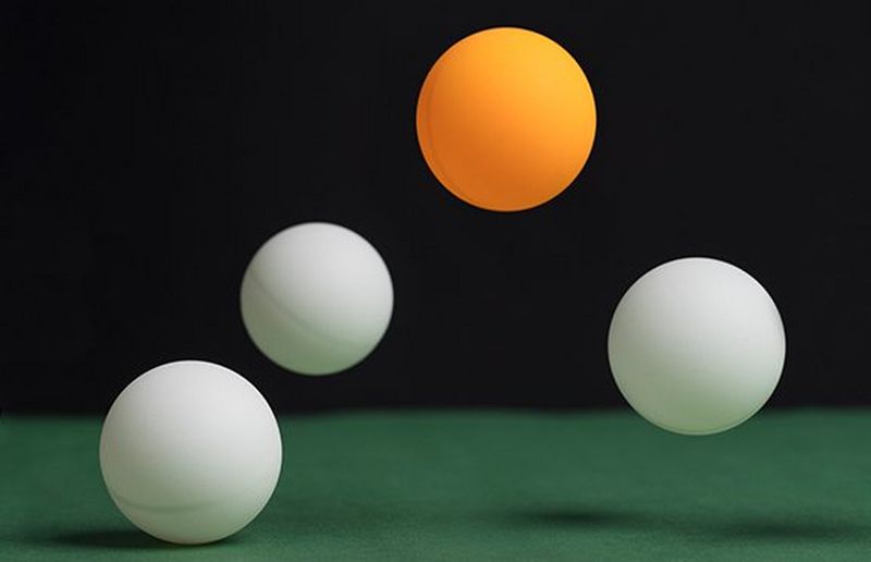 Balls bouncing on a table, one is orange the rest are white