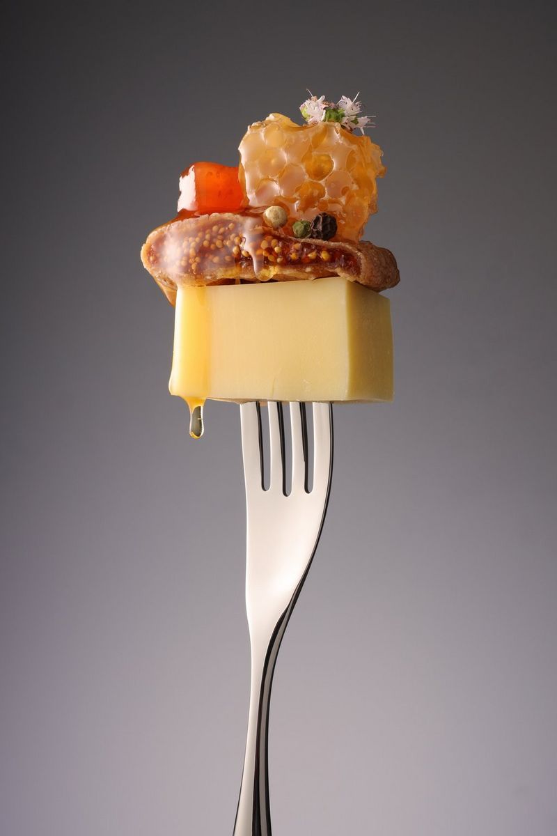 Кусочек сыра, инжир и фрукты на вилке, направленной зубчиками вверх.