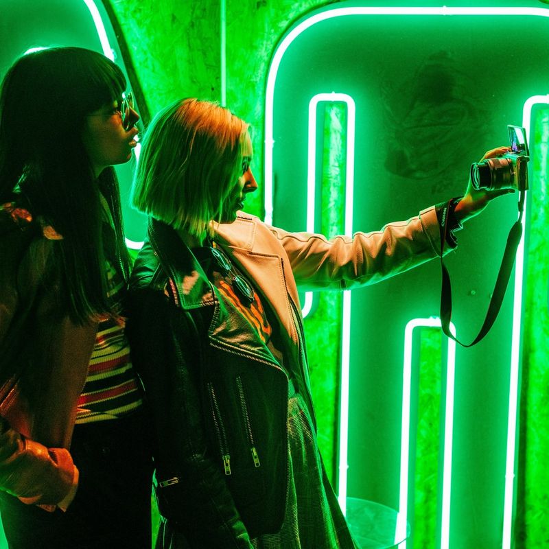 Canon EOS M100 Weiß + EF-M 15-45mm f/3.5-6.3 IS STM Objektiv Silber 0 Eine Frau, die sich mit einem SELPHY vor einem neonfarbenen Hintergrund fotografiert