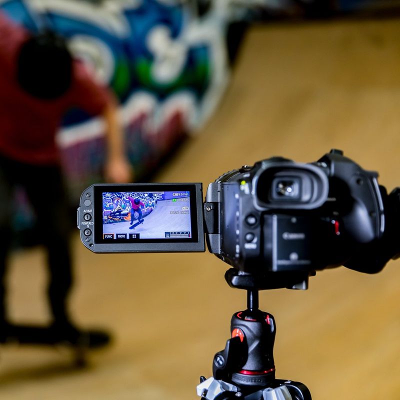 Canon LEGRIA GX10 Rückansicht von links mit ausgeklapptem Bildschirm auf einem Stativ