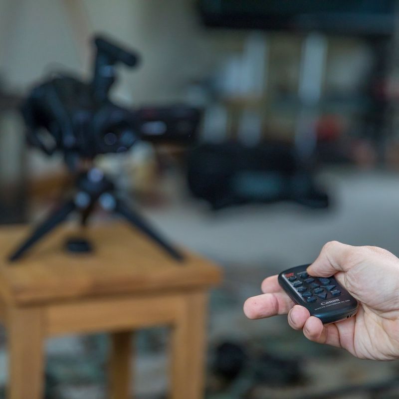 Canon LEGRIA GX10 Fernauslöser in einer Hand mit verschwommener Kamera im Hintergrund