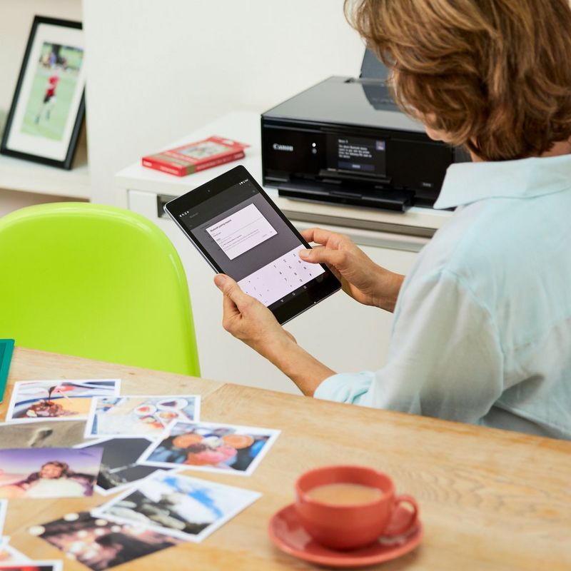 Canon PIXMA TS9150 – Dunkelgrau Auf einem Tisch neben einer Person, die ein Smartphone nutzt