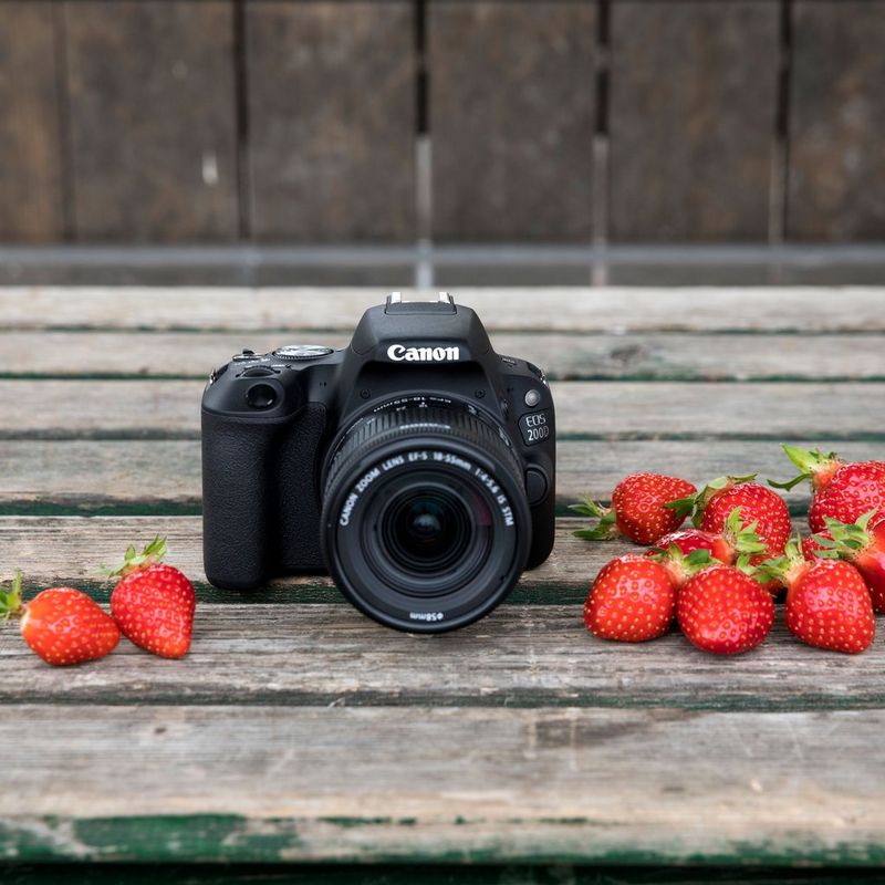 Canon EOS 200D Gehäuse – Schwarz Kamera auf einem Tisch mit Erdbeeren auf beiden Seiten