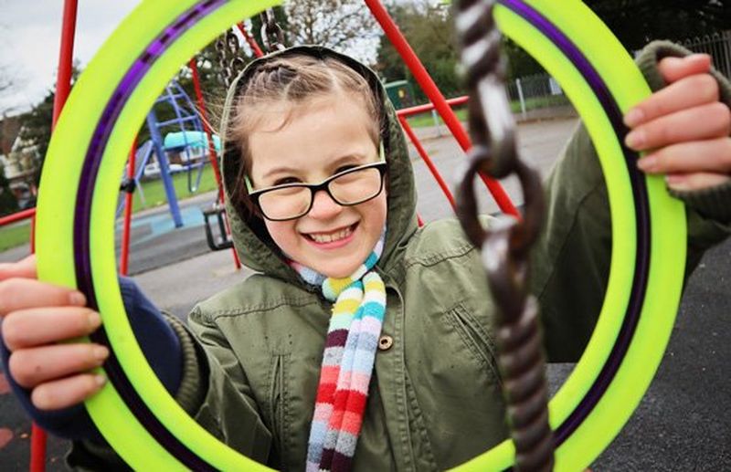 A girl holds a frisbee in front of her like a picture frame around her face.