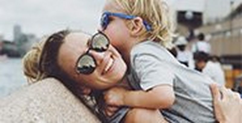 A mother picks her son up to hug, both of them wearing sunglasses.