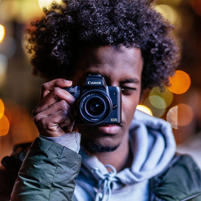 Canon EOS M50 Schwarz + EF-M 15-45mm IS STM Objektiv Schwarz 0 Ein Mann, der die Kamera vor sein Gesicht hält