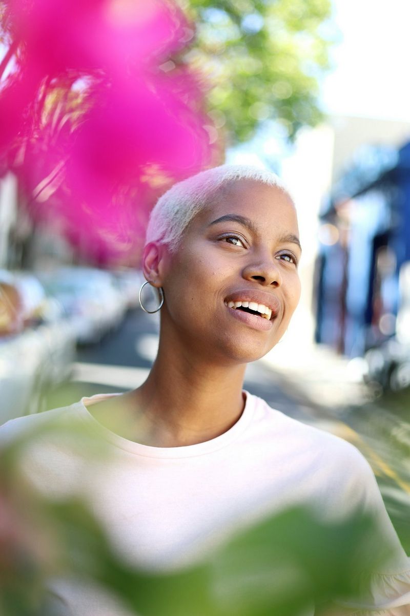 A portrait of a smiling woman with foreground foliage and background detail both out of focus.