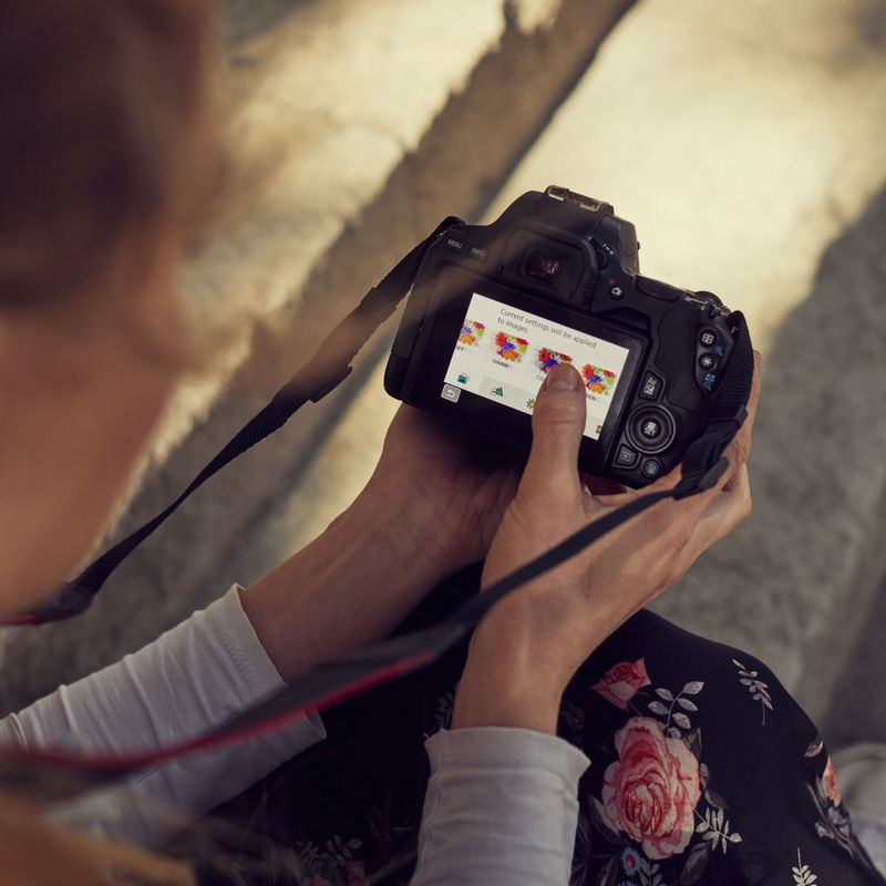 Canon EOS 250D Gehäuse, Silber + EF-S 18-55mm f/4-5.6 IS STM Objektiv Frau, die Einstellungen an ihrer Kamera ändert