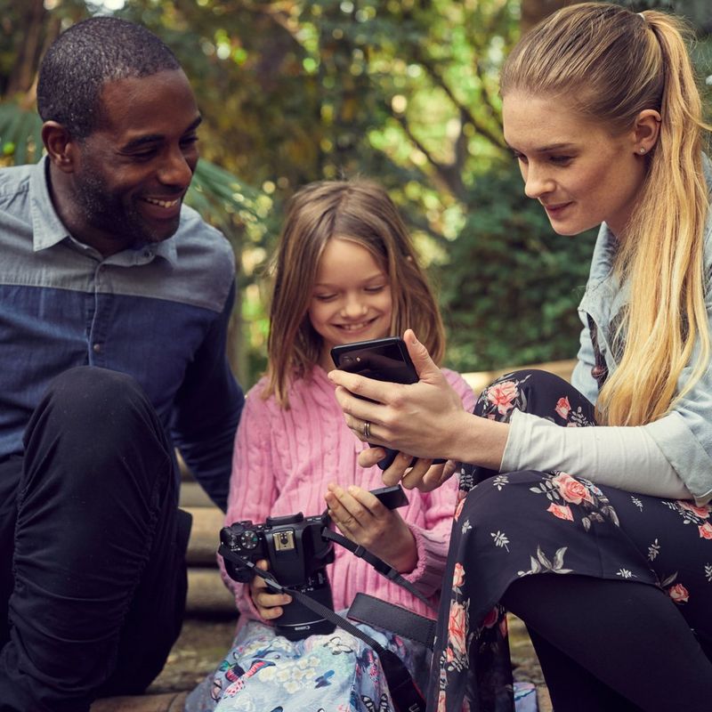 Canon EOS 250D Gehäuse, Silber + EF-S 18-55mm f/4-5.6 IS STM Objektiv Familie, die ein Foto auf einem Mobiltelefon ansieht