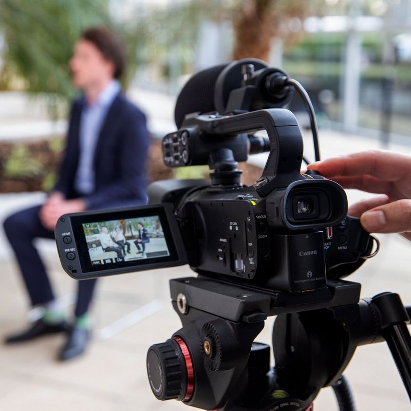 Canon XA45 Camcorder Rückansicht von links beim Filmen auf einem Stativ mit umgeklapptem Bildschirm