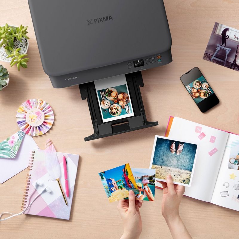 Canon PIXMA TS5350 Tintenstrahl-Multifunktionssystem, Schwarz Produkt Ansicht von oben mit einem ausgeklappten Papierfach und einer Person, die die Fotos prüft