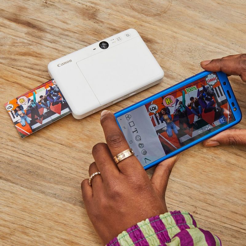 Canon Zoemini S Sofortbildkamera und Mini-Fotodrucker, Perlweiß Drucker, aus dem ein Druck kommt, zusammen mit einer Kamera auf einem Tisch