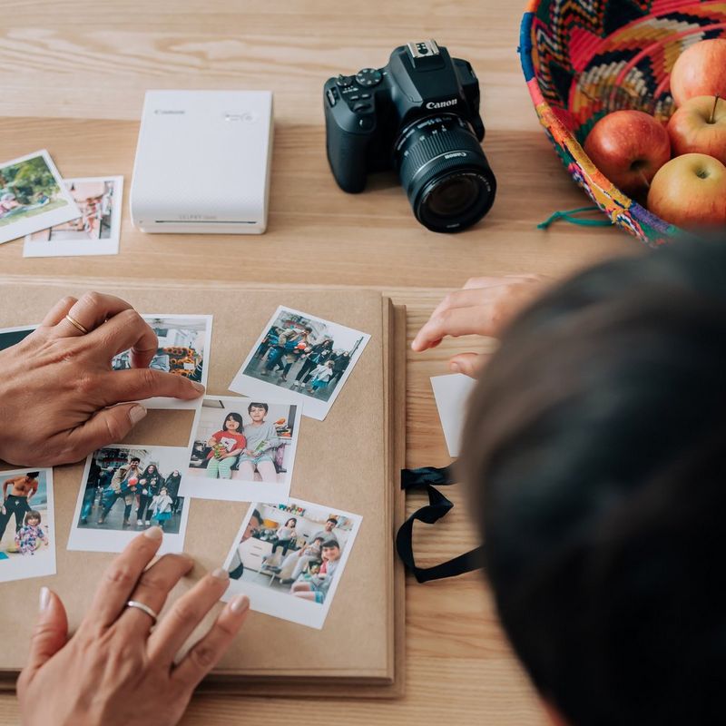 Canon SELPHY SQUARE QX10 mobiler WLAN-Farbfotodrucker, Premium-Kit, Weiß Hände, die Fotos in ein Album kleben