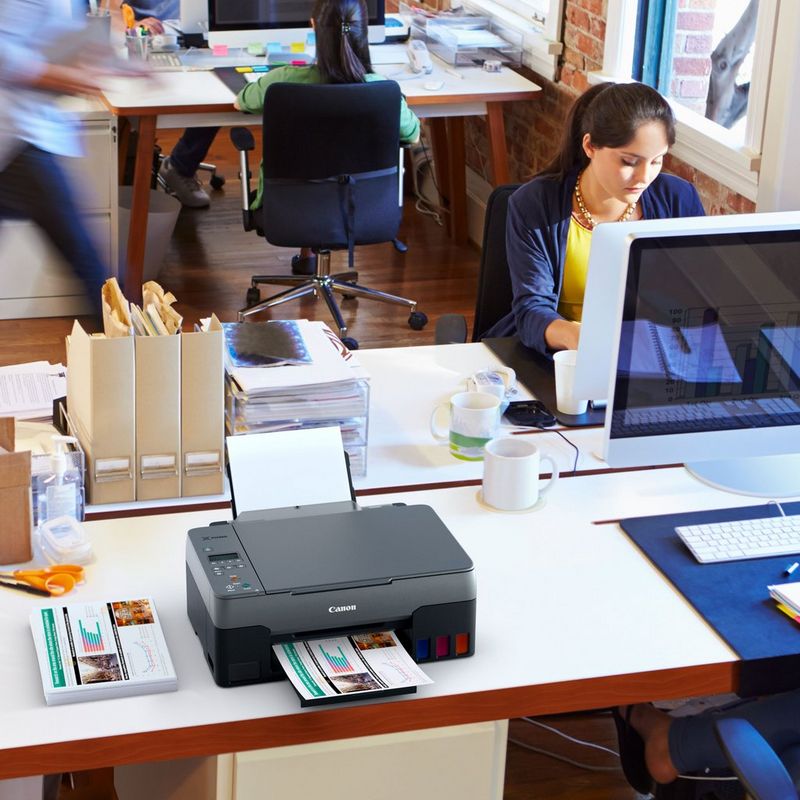 Canon PIXMA G2520 3-in-1 MegaTank Farbdrucker mit nachfüllbaren Tintenbehältern Auf einem Bürotisch neben einem Desktop-PC und mit ausgeklapptem Papierfach und Papierstütze