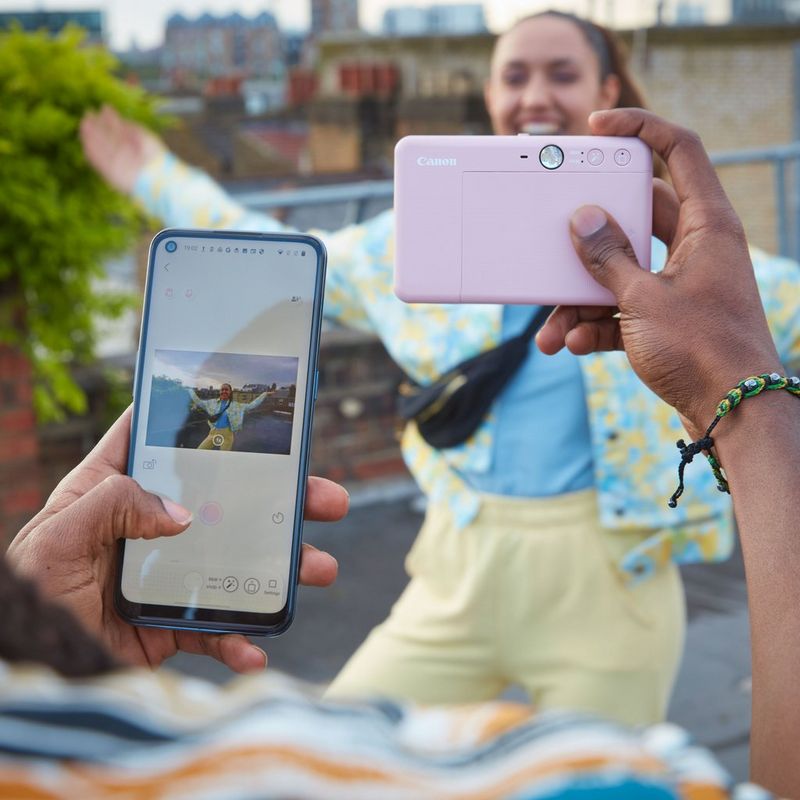 Canon Zoemini S2 Sofortbildkamera mit Mini-Farbfotodrucker, Roségold Hand knipst den Drucker und benutzt dabei das Handy