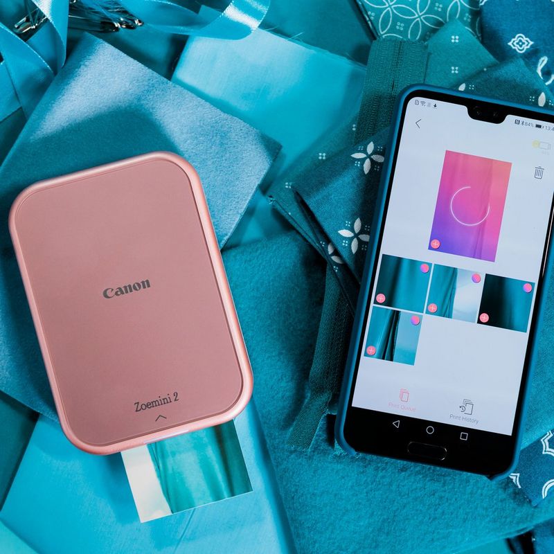 Canon Zoemini 2 tragbarer Farbfotodrucker, roségold + 20 Blatt 5 x 7,6 cm ZINK™ Fotopapier + 10 Blatt 3,3 cm ZINK™ rundes Stickerpapier Mobiltelefon neben dem Produkt