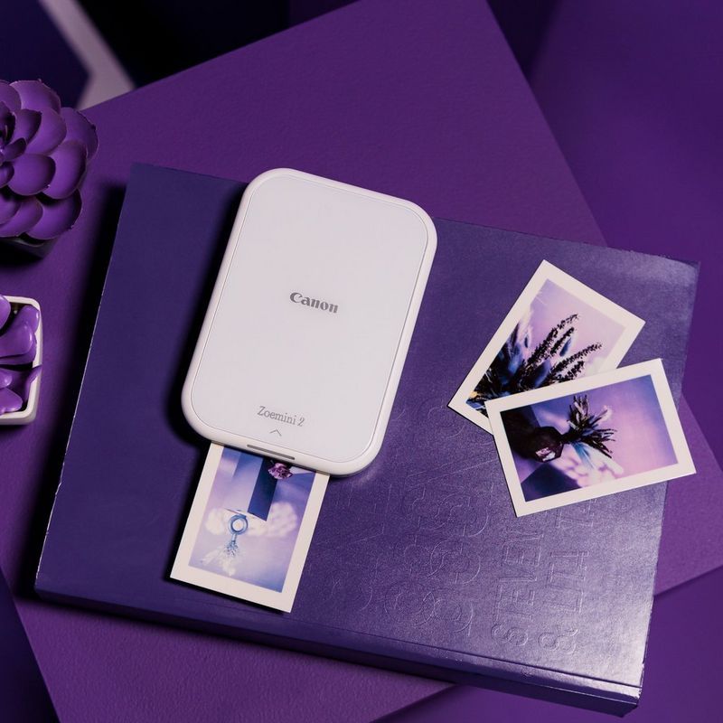 Canon Zoemini 2 tragbarer Farbfotodrucker, weiß + 20 Blatt 5 x 7,6 cm ZINK™ Fotopapier + 10 Blatt 3,3 cm ZINK™ rundes Stickerpapier Produkt auf einem blauen Tagebuch