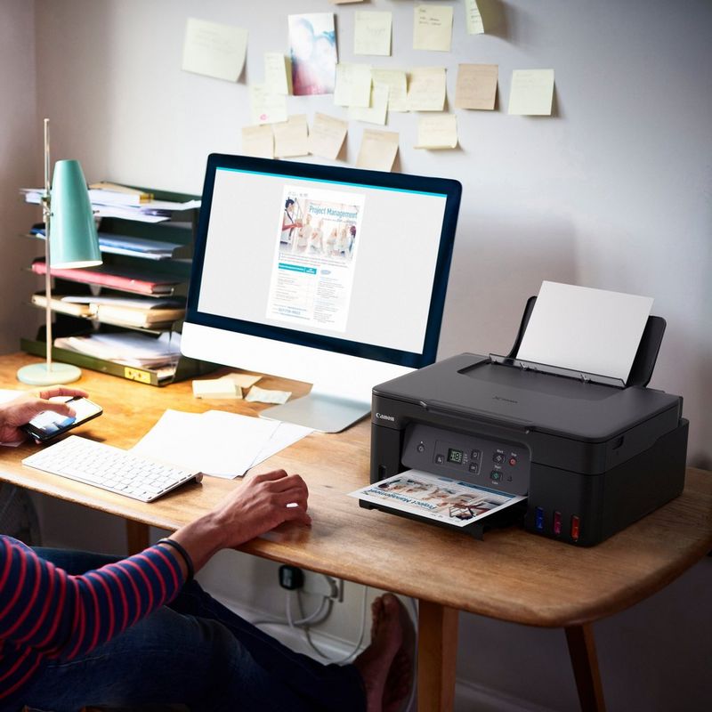 Canon PIXMA G2570 3-in-1 MegaTank Farbdrucker mit nachfüllbaren Tintenbehältern Produkt auf einem Schreibtisch, an dem eine Frau an einem Computer arbeitet