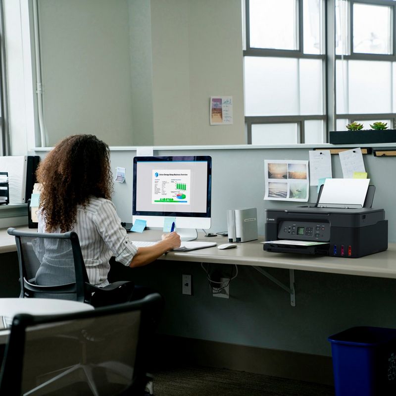 Canon PIXMA G3570 WLAN 3-in-1 MegaTank Farb-Multifunktionssystem mit nachfüllbaren Tintentanks , Schwarz Produkt auf einem Schreibtisch, an dem eine Frau an einem Computer arbeitet