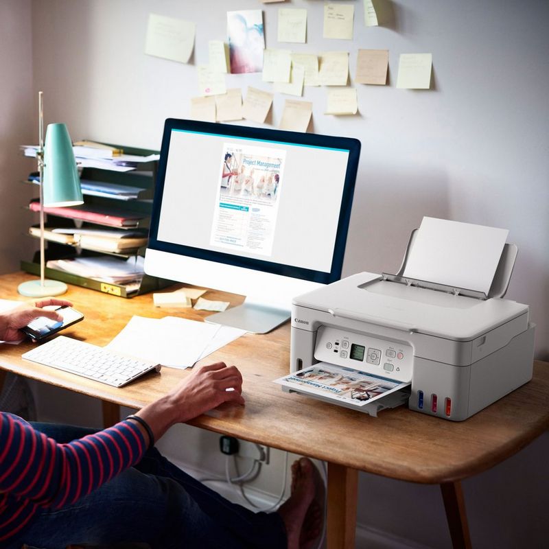 Canon PIXMA G3571 MegaTank 3-in-1 Farb-Multifunktionssystem mit WLAN und nachfüllbaren Tintentanks, Weiß Produkt auf einem Schreibtisch, an dem eine Frau ein Telefon in der Hand hält